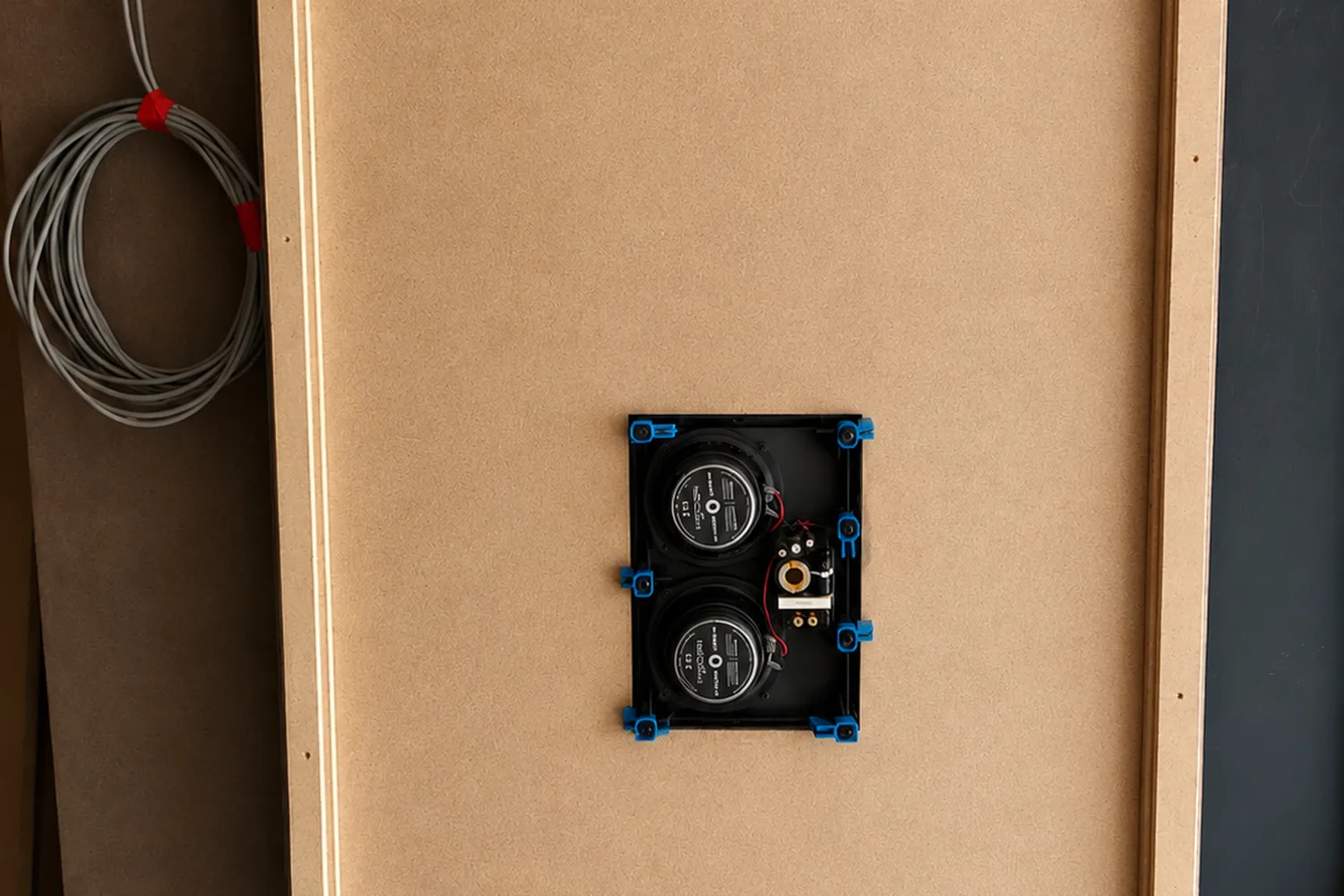 Surround speaker mounted into an acoustic side-wall panel, with speaker cable dressed and coiled behind the panel