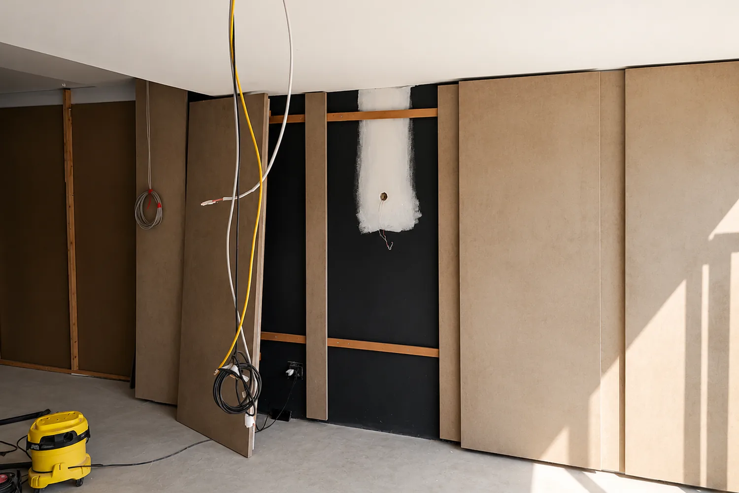 Modco acoustic wall panels being fitted over the dampened substrate, with cabling dressed behind